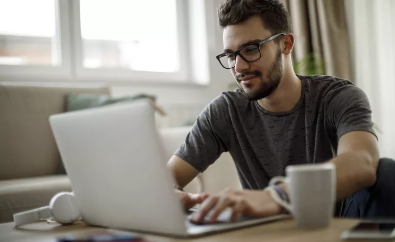 A young man types on his laptop at his kitchen table. A young man types on his laptop at his kitchen table.