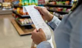 Shopper holding a long grocery receipt in a supermarket aisle.